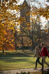 two students walking on central campus with campanile in the background and yellow fall leaves in the foreground