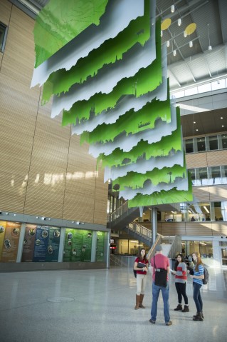 Four students gather under the large hanging art piece in the ABE building.