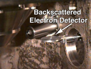 This image shows the inside of the sample chamber. On the far left of the backscatter detector is the lens, in the center is the secondary detector. To collect electrons, the backscatter detector moves under the lens so the electron beam can travel through the hole in its center.